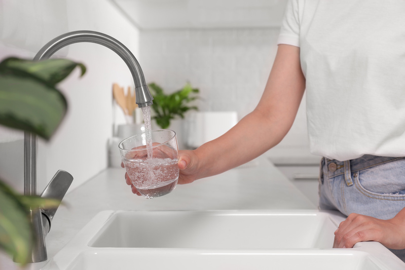 Woman filling glass with filtered water from tap in kitchen