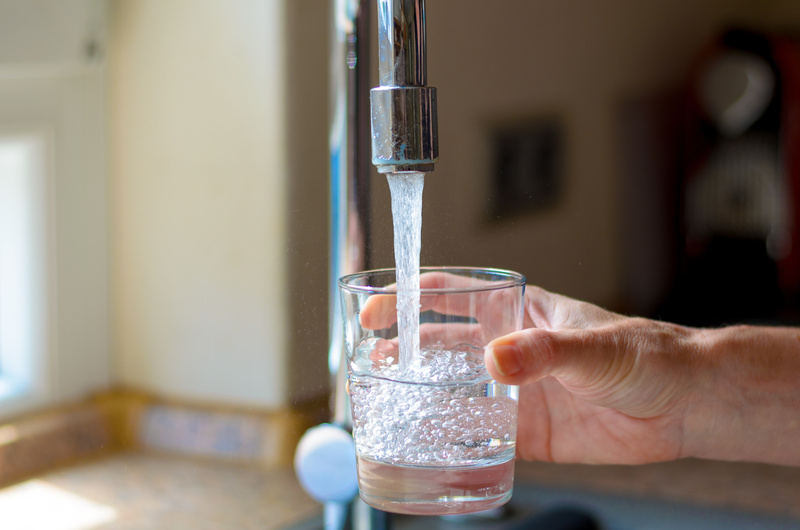 Woman filling a glass of water from a stainless steel or chrome tap or faucet, close up on her hand and the glass with running conditioned water